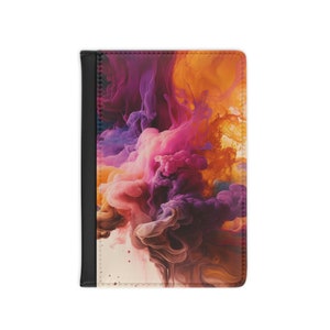 Peut inclure: Une housse de passeport avec un design abstrait coloré présentant des nuances tourbillonnantes de rose, violet, orange et marron. La housse a une bordure en cuir noir.