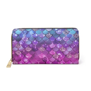 May include: A rectangular wallet with a mermaid scale pattern in shades of blue, purple, and pink. The scales are embellished with glitter accents. The wallet has a gold-colored zipper and pull.