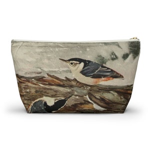 May include: A white zippered pouch with a watercolor illustration of two birds perched on a branch. The birds are black, white, and red with a snowy background.