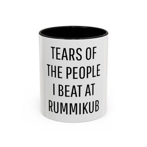 May include: White ceramic mug with a black interior. The mug features the text "TEARS OF THE PEOPLE I BEAT AT RUMMIKUB" in bold black letters. A humorous gift for Rummikub players.