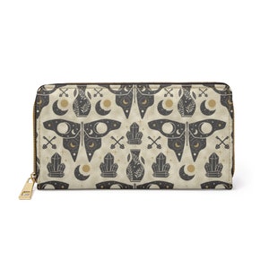 May include: A beige zippered wallet with a repeating pattern of black moths, crystals, vases, and moons. The pattern is on a textured background.