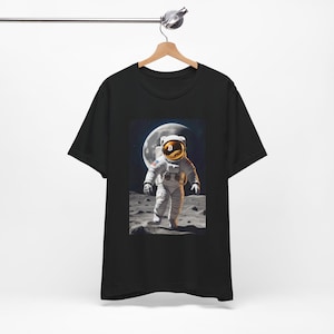 May include: Black t-shirt featuring a graphic of an astronaut on the moon with a Bitcoin symbol on their helmet.
