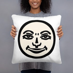 May include: White cushion with a black and white illustration of a face with a circle around it.