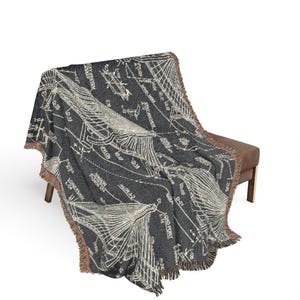 May include: A dark charcoal gray woven throw blanket featuring a white technical architectural blueprint design of a bridge structure with various labels, technical annotations, and structural diagrams, finished with a fringed edge detail.