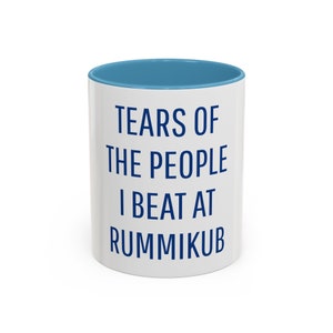 May include: White ceramic mug with a blue rim. The mug has the text "Tears of the people I beat at Rummikub" printed in blue.