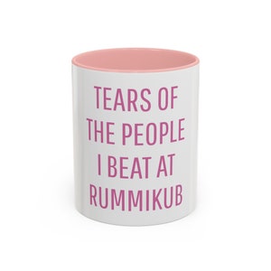 May include: White ceramic mug with a pink rim. The mug has pink text that reads "Tears of the people I beat at Rummikub".