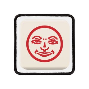 Op de afbeelding: Een witte vierkante patch met een zwarte rand. De patch heeft een rode cirkel met een gestileerd gezicht erin. Het gezicht heeft twee ogen, een neus en een mond.