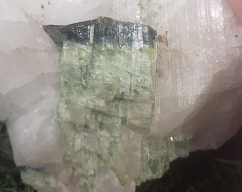 May include: A large, rough quartz crystal with a section of green tourmaline. The tourmaline has a layered, crystalline structure with a dark top layer. The quartz is a milky white colour.