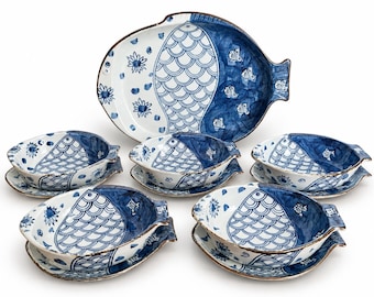 May include: A ceramic dinnerware set featuring a large fish-shaped serving platter and four matching fish-shaped bowls, all decorated with a blue and white hand-painted fish scale pattern, floral accents, and small fish motifs.