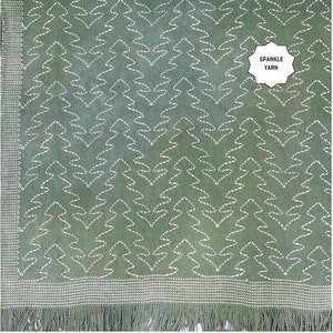 Peut inclure: Une couverture en tissu vert avec un motif brodé blanc de sapins stylisés. La couverture a une bordure en franges et les mots "Sparkle Yarn" sont imprimés sur une étiquette blanche.