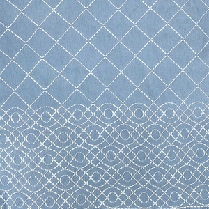 Può includere: Una coperta blu con un motivo a rombi bianchi e un motivo a onde bianche lungo il bordo inferiore. La coperta ha un bordo a frangia.