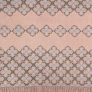 Peut inclure: Une couverture en laine rose tissée avec un motif géométrique bleu et marron. La couverture a une bordure en franges.