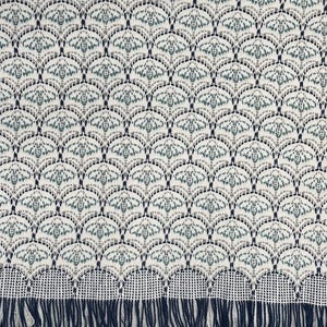 Puede incluir: Textil color crema con un patrón repetido de motivos de abeja estilizados en tonos grises y verde azulado. El diseño está dispuesto en un patrón de escamas. El borde inferior presenta una franja azul marino.