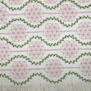 May include: White fabric with a pink and green embroidered design. The design features repeating circles with a floral pattern and green vines.