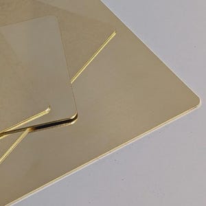 Könnte beinhalten: Ein Satz goldfarbener Visitenkartenhalter aus Metall und eine größere rechteckige Ablage. Die Artikel sind auf einer weißen Oberfläche angeordnet, wobei sich die Karten mit der Ablage überlappen. Das Metall hat eine reflektierende Oberfläche.