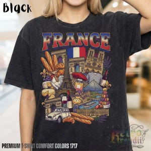 A person wearing a black acid-wash T-shirt featuring a colorful graphic design of France landmarks and symbols, including the Eiffel Tower, Notre-Dame, croissants, wine, and French fashion, showcasing European culture.
