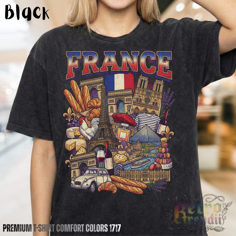 A person wearing a black acid-wash T-shirt featuring a colorful graphic design of France landmarks and symbols, including the Eiffel Tower, Notre-Dame, croissants, wine, and French fashion, showcasing European culture.