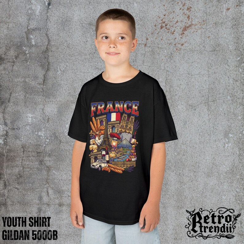 A young boy wearing a black T-shirt featuring a colorful graphic design of France landmarks and symbols, including the Eiffel Tower, Notre-Dame, croissants, wine, and French fashion.