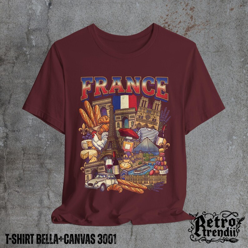 A Red T-shirt featuring a colorful graphic design of France landmarks and symbols, including the Eiffel Tower, Notre-Dame, croissants, wine, and French fashion, displayed on a textured grey background.