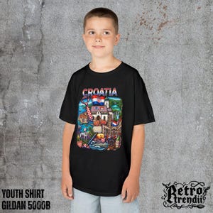 A young boy wearing a black T-shirt featuring a colorful graphic design of Croatia landmarks and symbols, including a Dalmatian dog, necktie, Mediterranean coast, and historic architecture.