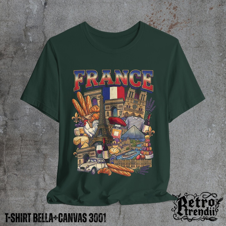 A Green T-shirt featuring a colorful graphic design of France landmarks and symbols, including the Eiffel Tower, Notre-Dame, croissants, wine, and French fashion, displayed on a textured grey background.