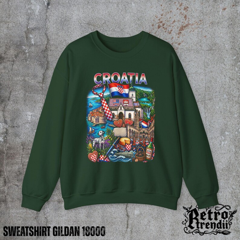 A Green crewneck sweatshirt featuring a detailed graphic design of Croatia landmarks and symbols, including a Dalmatian dog, necktie, Mediterranean coast, and historic architecture, displayed on a textured grey background.