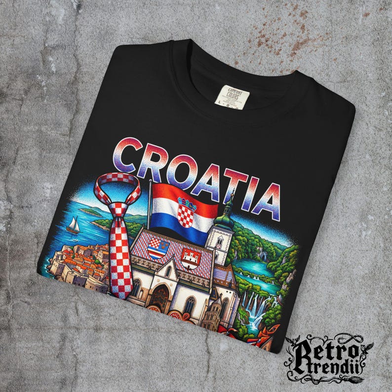 A black acid-wash T-shirt featuring a colorful graphic design of Croatia landmarks and symbols, including a Dalmatian dog, necktie, Mediterranean coast, and historic architecture, showcasing European culture.