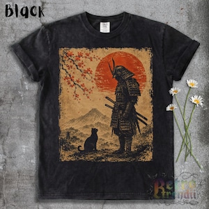 May include: A black t-shirt featuring a graphic print of a samurai standing before a large red sun, a mountain, and a black cat. A branch with orange leaves hangs above the samurai. The word Black is printed in the top left corner of the image.