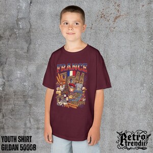 A young boy wearing a Red T-shirt featuring a colorful graphic design of France landmarks and symbols, including the Eiffel Tower, Notre-Dame, croissants, wine, and French fashion.