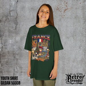A young girl wearing a green T-shirt featuring a colorful graphic design of France landmarks and symbols, including the Eiffel Tower, Notre-Dame, croissants, wine, and French fashion.