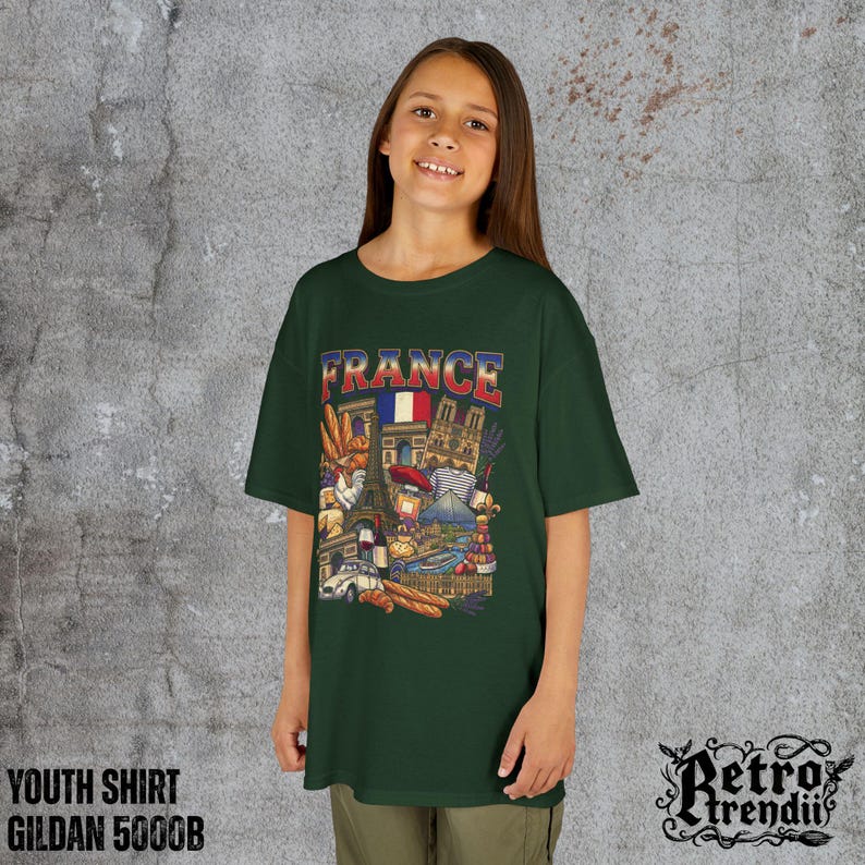 A young girl wearing a green T-shirt featuring a colorful graphic design of France landmarks and symbols, including the Eiffel Tower, Notre-Dame, croissants, wine, and French fashion.