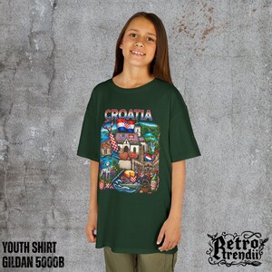 A young girl wearing a Green T-shirt featuring a colorful graphic design of Croatia landmarks and symbols, including a Dalmatian dog, necktie, Mediterranean coast, and historic architecture.
