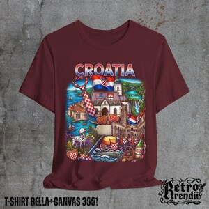 A Red T-shirt featuring a colorful graphic design of Croatia landmarks and symbols, including a Dalmatian dog, necktie, Mediterranean coast, and historic architecture, displayed on a textured grey background.