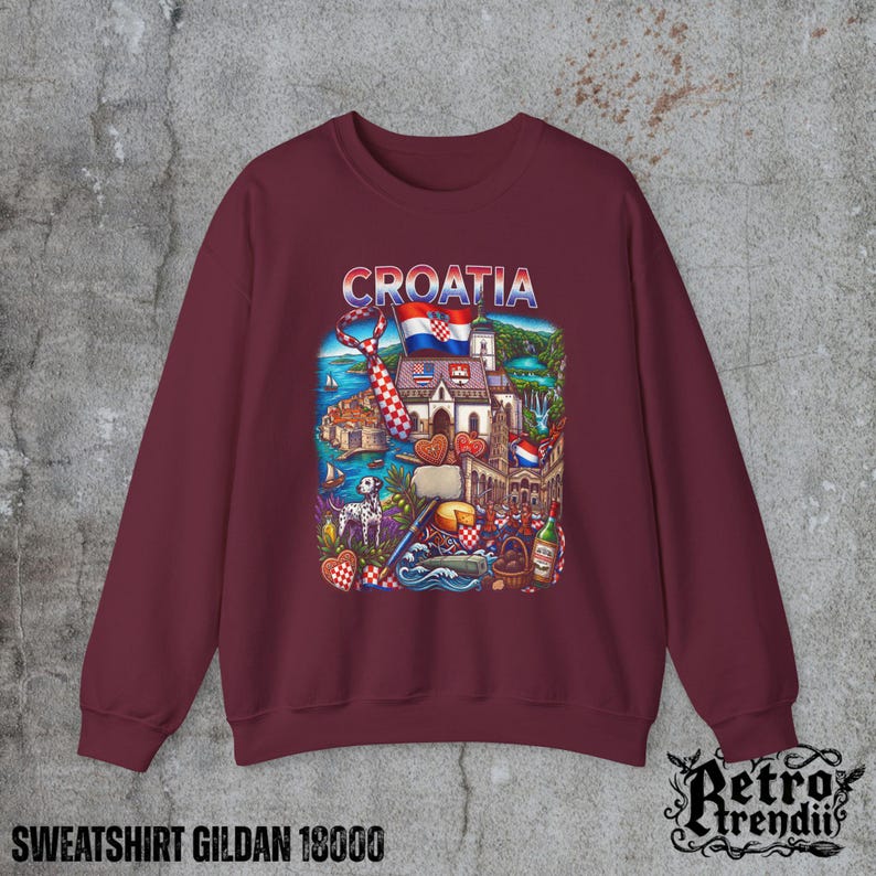 A Red crewneck sweatshirt featuring a detailed graphic design of Croatia landmarks and symbols, including a Dalmatian dog, necktie, Mediterranean coast, and historic architecture, displayed on a textured grey background.