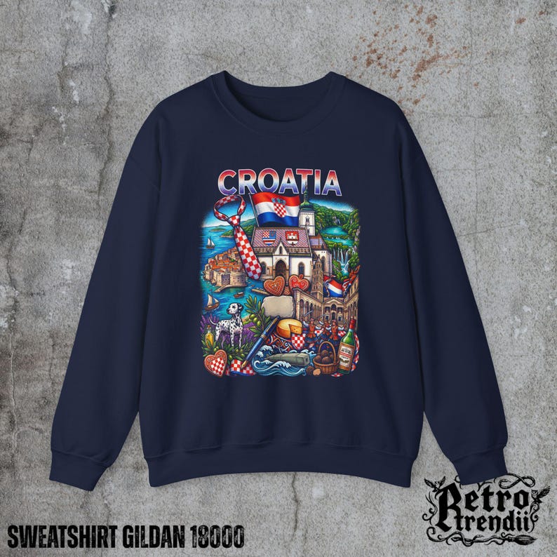 A blue crewneck sweatshirt featuring a detailed graphic design of Croatia landmarks and symbols, including a Dalmatian dog, necktie, Mediterranean coast, and historic architecture, displayed on a textured grey background.