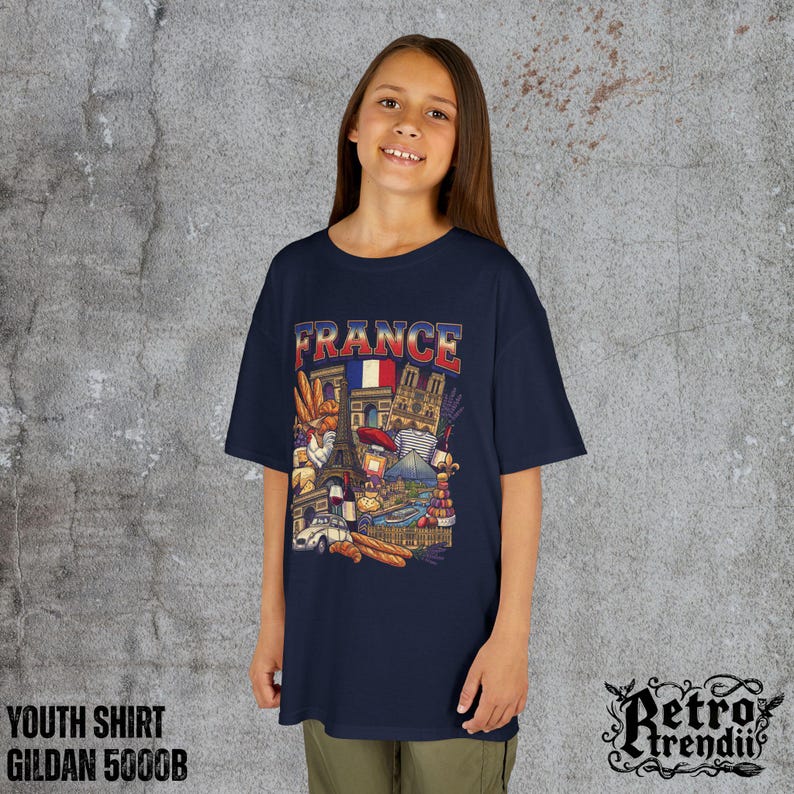 A young girl wearing a blue T-shirt featuring a colorful graphic design of France landmarks and symbols, including the Eiffel Tower, Notre-Dame, croissants, wine, and French fashion.