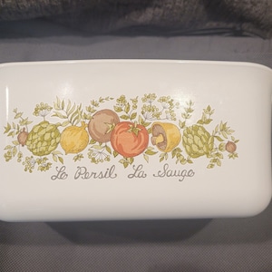 May include: White ceramic casserole dish with a green, yellow, and orange floral design and the text "Le Persil La Sauge".
