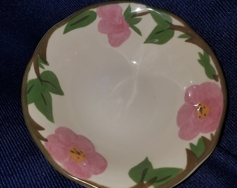 May include: A white ceramic bowl with a pink and green floral design. The bowl has a scalloped edge and is perfect for serving snacks or desserts.
