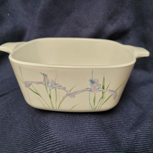 May include: White ceramic baking dish with a square shape and two handles. The dish has a floral design featuring blue and purple irises with green leaves.