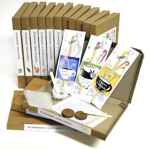 Könnte beinhalten: Ein Set aus 10 braunen Kartons mit bunten Etiketten und verschiedenen Saatgutpaketen. Die Etiketten auf den Kartons lauten "Kit Germinazione - Coltiva il tuo orto", was mit "Saatgut-Set - Baue deinen Garten an" übersetzt werden kann. Die Saatgutpakete haben verschiedene Designs und Botschaften, wie "Keep Calm", "Peace and Love" und "I have a dream".