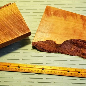 Puede incluir: Dos piezas de madera sin terminar con bordes naturales, una rectangular y otra con una forma orgánica única. Una regla de madera amarilla está cerca. La madera muestra tonos marrones cálidos y patrones de vetas visibles, para proyectos de carpintería.