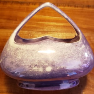 May include: A purple ceramic planter with a heart-shaped opening and a white speckled glaze. The planter has a handle on the top and a wide base.