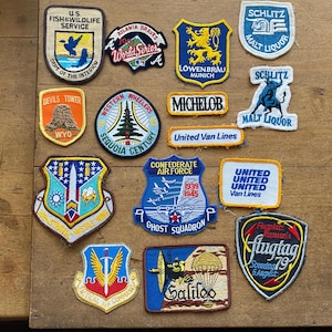 May include: A collection of embroidered patches with various designs and text. Patches include logos for the Atlanta Braves, Löwenbräu, and the U.S. Fish & Wildlife Service. Other patches feature text like "Michelob" and "Galileo."