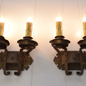 May include: A pair of antique wrought iron wall sconces with two candle-style light bulbs each. The sconces have a dark brown finish and intricate scrollwork.