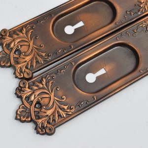 May include: Two antique brass door plates with ornate floral designs and keyhole cutouts.