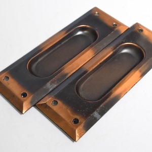 May include: Two antique-style door pulls with a black and copper finish. The pulls have a rectangular shape with an oval cutout in the center.