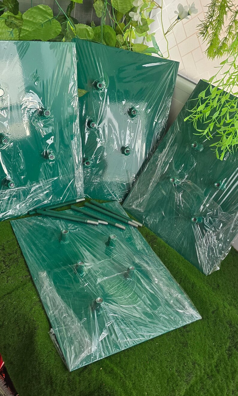 May include: Several dark green rectangular panels, wrapped in clear plastic, with metal hardware visible. The panels are arranged on a green surface, with additional metal rods. The items appear to be components for a decorative or structural project.
