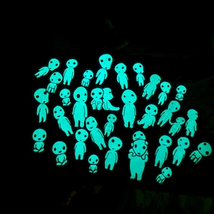 May include: A collection of numerous small, glow-in-the-dark figures arranged against a solid black background. Each figure features a smooth, rounded head with simple facial features, emitting a bright cyan light in the darkness.