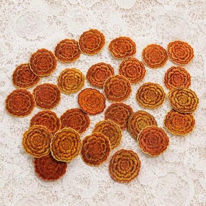 May include: A collection of numerous circular embroidered patches featuring a detailed floral design in shades of orange, gold, and brown. Each patch displays a dense, layered petal pattern with a scalloped edge, creating a uniform appearance.
