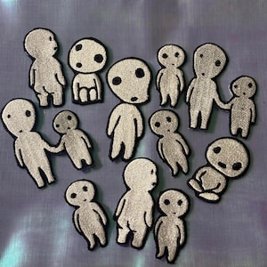 May include: A collection of twelve embroidered patches featuring stylized white figures with large round heads and black circular eyes. The figures are depicted in various poses, including standing, sitting, and holding hands, all outlined in black thread.